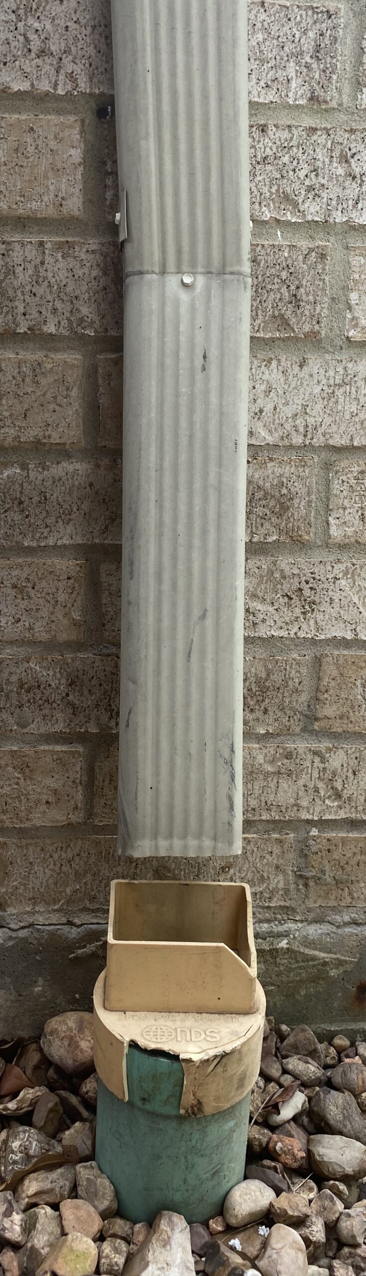 Downspout connection routing water safely into a drain line beside a home