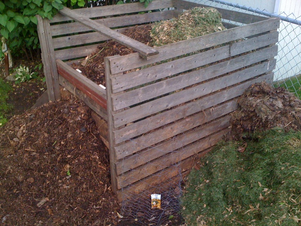 A simple wooden compost bin in an outdoor garden setting.
